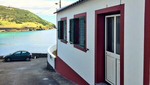 Un bâtiment situé sur la côte, avec une voiture garée devant, une vue dégagée sur la mer et un paysage vallonné en arrière-plan.