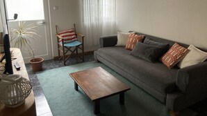 Un salon avec un canapé gris, une table basse en bois, un fauteuil à rayures et une plante en pot.