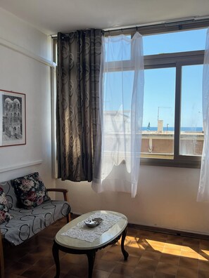 A room with a sofa, a table with a bowl and a lace doily, a window with curtains, and a framed picture on the wall.