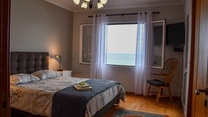 Quarto com cama, poltrona, televisão e janela com vista para o mar.
