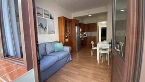 A living room with a sofa, a dining table with chairs, and a kitchen area with cabinets and appliances.