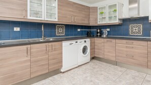 Une cuisine moderne avec des meubles en bois, un lave-linge encastré et un dosseret de carrelage bleu.