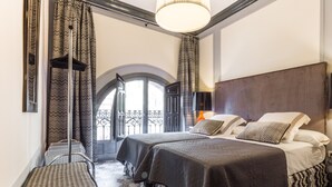 Habitación de hotel con dos camas, un ventanal con vistas, una araña y baldosas de suelo estampadas.