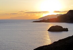 A coastal sunset with calm waters and rocky terrain.