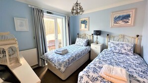 Une chambre avec deux lits, un lustre, un tableau encadré et un panneau indiquant la sortie de secours.