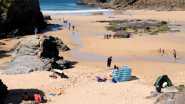Une plage avec des gens, des tentes et une côte rocheuse.