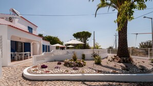 A white building with blue shutters, a paved courtyard with a garden, and outdoor seating. - Casa do Farol – Cozy Retreat with Special Rates in Low Season Algarve (Carvoeiro)