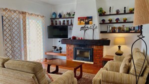 A living room with a fireplace, sofas, a coffee table, and decorative shelves. - Casa do Farol – Cozy Retreat with Special Rates in Low Season Algarve (Carvoeiro)