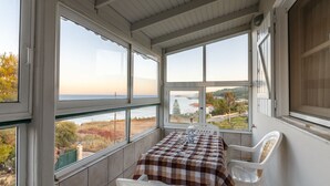 En balkon med bord og stole, store vinduer med udsigt over havet og landskabet, samt et hvidt loft.