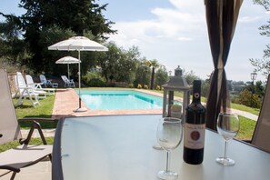 Une table placée au bord de la piscine, avec une bouteille de vin et deux verres, donnant sur une piscine entourée de chaises longues et de parasols.