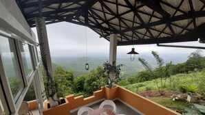 Une terrasse avec une table et des chaises, une lanterne suspendue et une vue sur un paysage luxuriant.