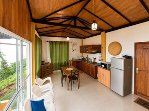 Une cuisine compacte avec un coin repas, des poutres en bois au plafond et une vue dégagée sur l’extérieur grâce à une grande fenêtre.