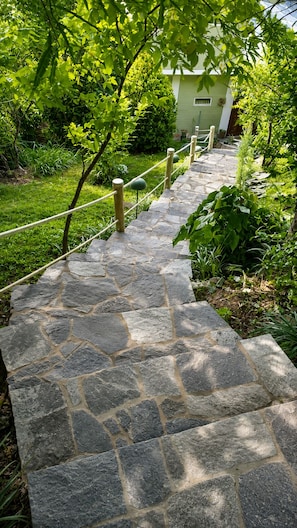 A stone staircase leading to a building with a green facade, surrounded by greenery.