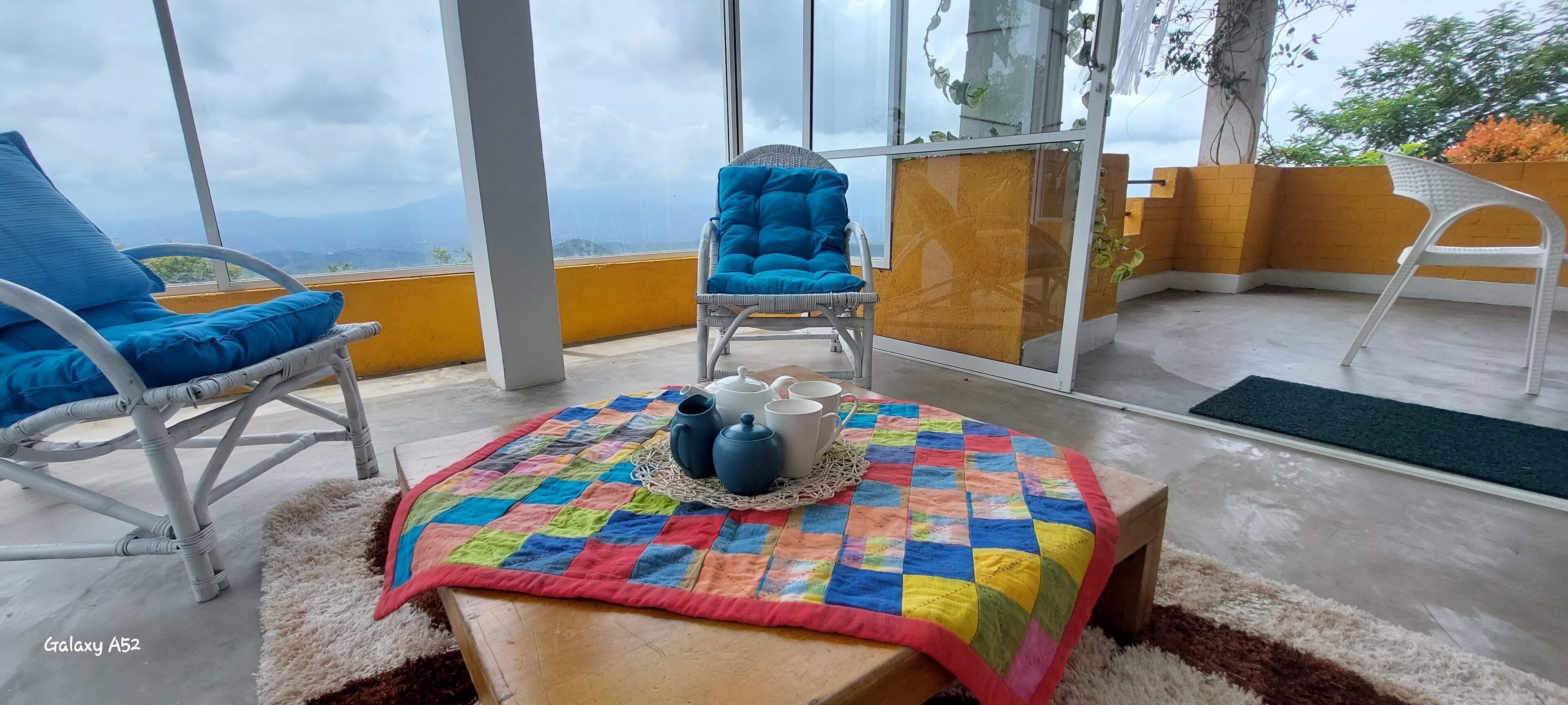 Un balcon avec des fauteuils en osier, une couverture aux couleurs vives et une table sur laquelle sont posées des théières.
