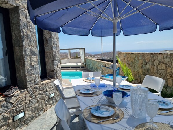 A table set for dining with a view of the sea and pool.
