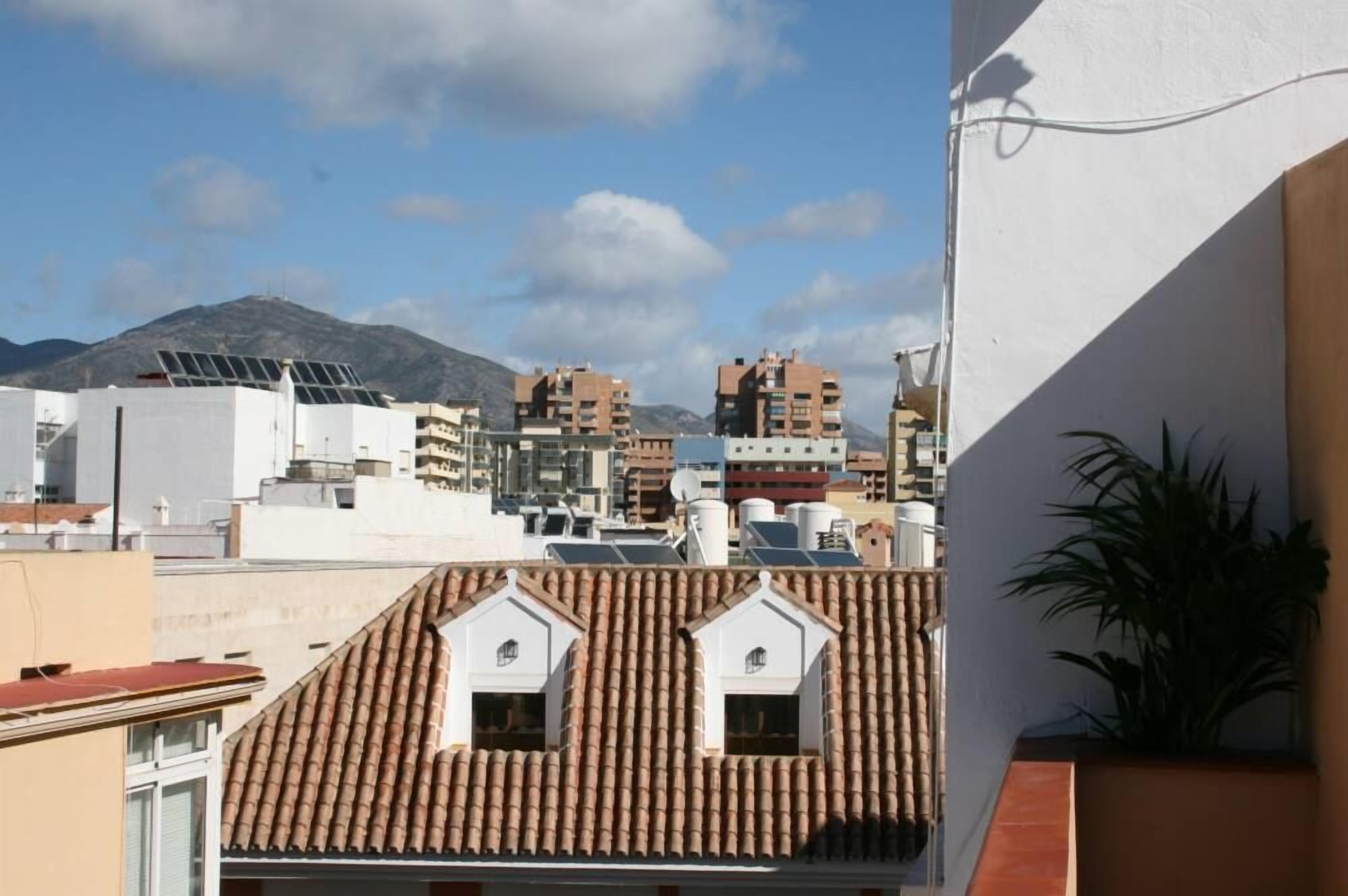 Zona residencial com telhados de telha de barro, uma montanha ao fundo e um edifício branco com painéis solares.