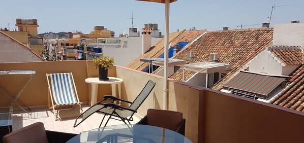 A rooftop terrace with a table, chairs, and a potted plant.