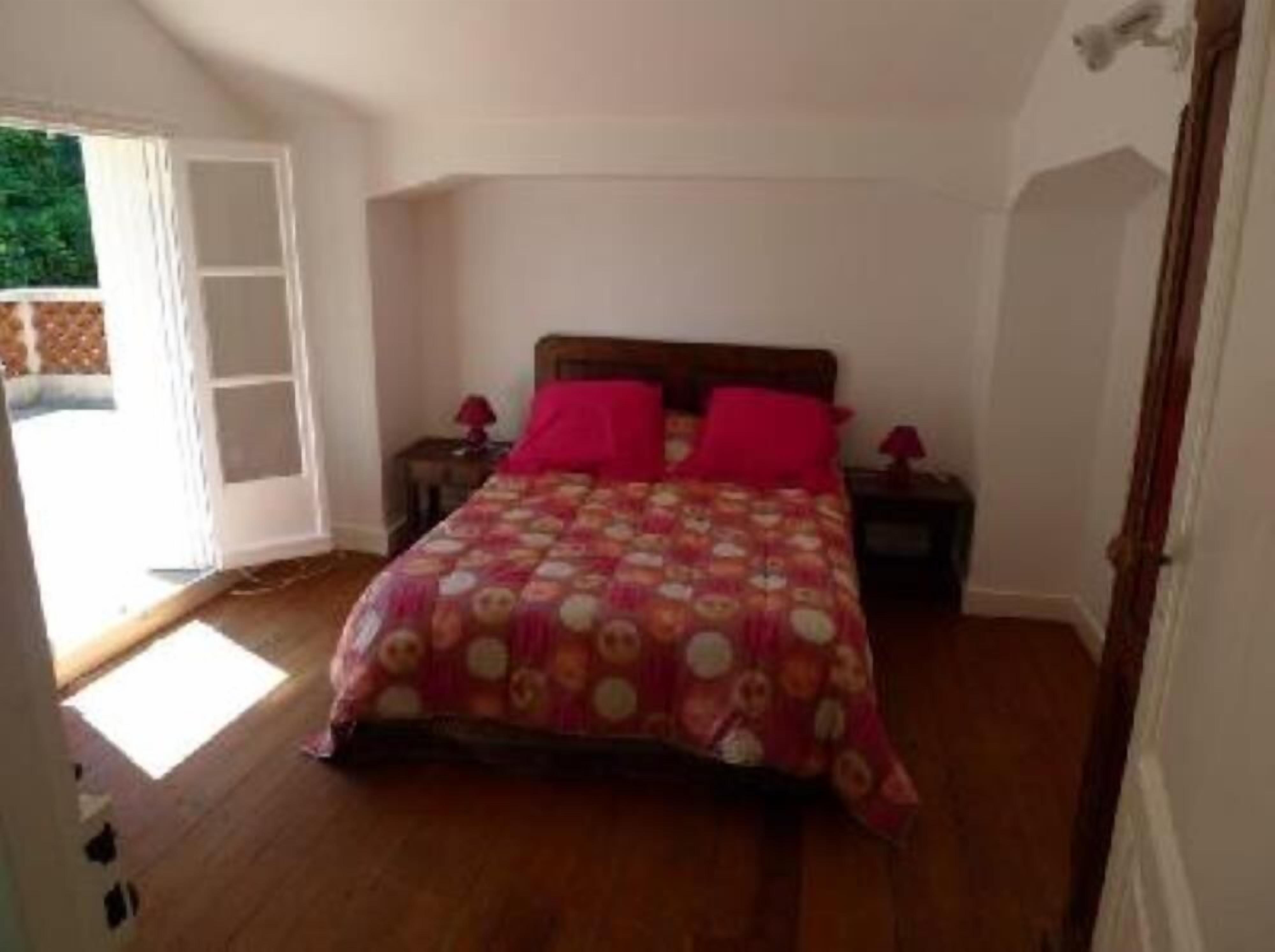 Quarto com cama de madeira, duas mesas de cabeceira e uma janela grande.