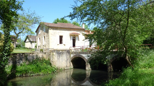 A stone bridge over a calm river, leading to a white building with a red roof. - Mansion - BERGERAC (Bergerac)