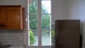 A kitchen with wooden cabinets, a stainless steel refrigerator, and a window with a view of greenery outside. - Mansion - BERGERAC (Bergerac)