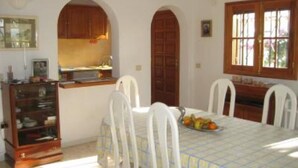 A dining area with a table set for four, white chairs, a fruit bowl, and a wooden cabinet with glass doors. - House / Villa with private pool (San Miguel de Abona)