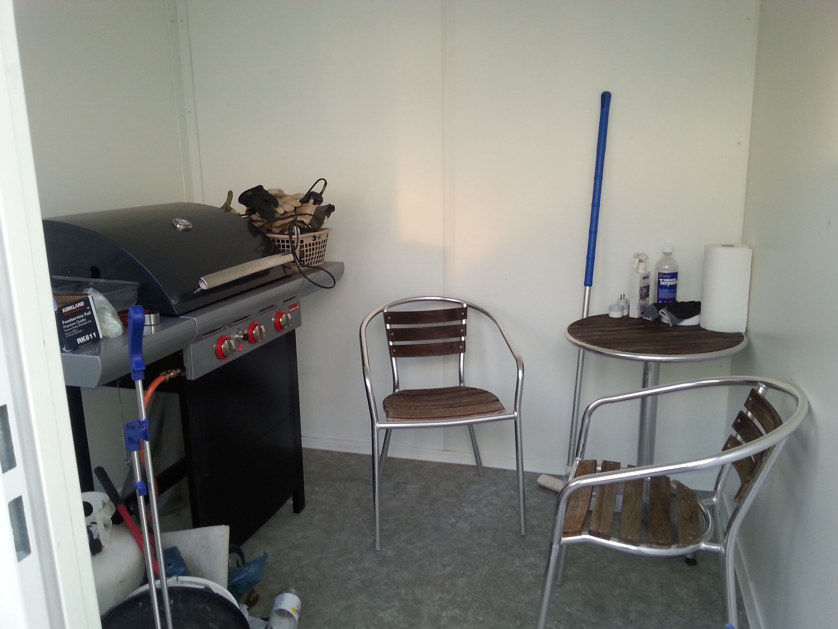 A compact room with a kitchenette, including a grill, a small table, two chairs, and a mop.