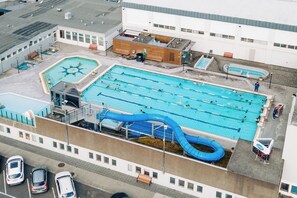 Vista aérea de um complexo de piscinas com várias piscinas, um toboágua azul e um edifício com telhado plano.