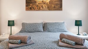 Une chambre d’hôtel avec un lit, deux lampes, un tableau représentant une scène historique et des serviettes.