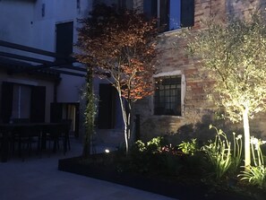 Ein Innenhof mit einem Steinhaus, einem Baum mit Herbstlaub und einem gut beleuchteten Gartenbereich.