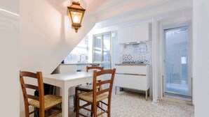 Une cuisine compacte avec des meubles blancs, un pare-feu en carreaux et un coin repas comprenant deux chaises en bois et une table blanche.