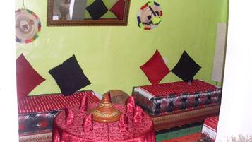Une chambre avec deux lits, une table rouge à motifs et un miroir au mur.