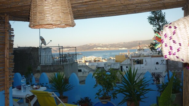 A terrace with a view of the sea, potted plants, and a hanging lamp.