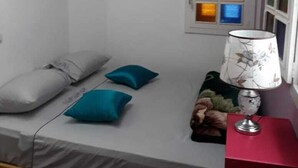 A small room with a bed, pillows, a lamp, and two windows with colorful panes.