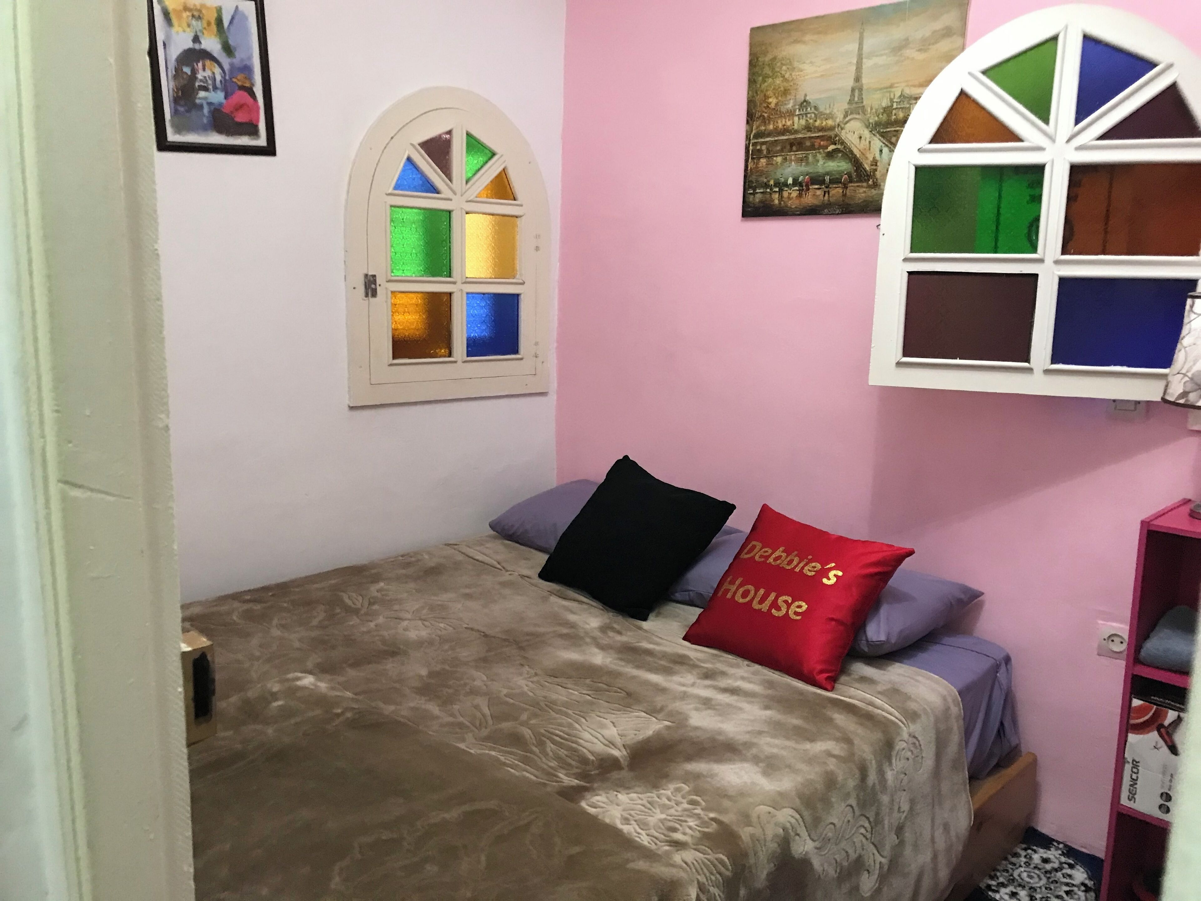A bedroom with a bed, a window with colored glass panes, and a pink wall.