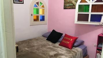 A bedroom with a bed, a window with colored glass panes, and a pink wall.