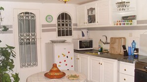 A kitchen with white cabinets, a microwave, a refrigerator, and a table with a Moroccan tagine.