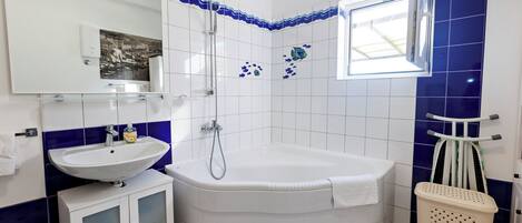 A bathroom with a bathtub, a sink, a mirror, and a window.