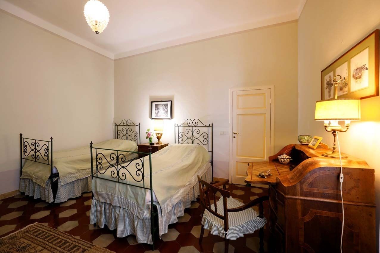 Une chambre avec deux lits, un bureau en bois, une chaise, une lampe et une porte.
