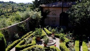 A garden with geometric hedges, a stone building, and a view of the surrounding landscape. - Villa with unique view of Siena with private pool (Ascarello)