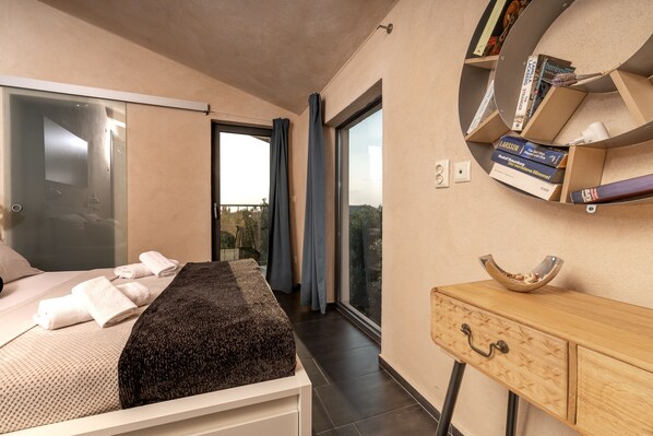 Un dormitorio moderno con cama, mesita de noche, un pequeño armario de madera y una estantería empotrada con libros.