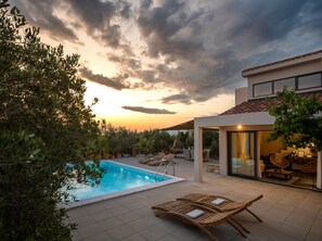 Un área de piscina con sillones de descanso, una zona de estar cubierta y vistas al atardecer.
