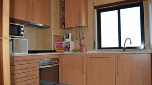 A compact kitchen with wooden cabinets, a microwave, a stove, and a window with a sink. -  Apartment sea view in Salgados Village (Guia)