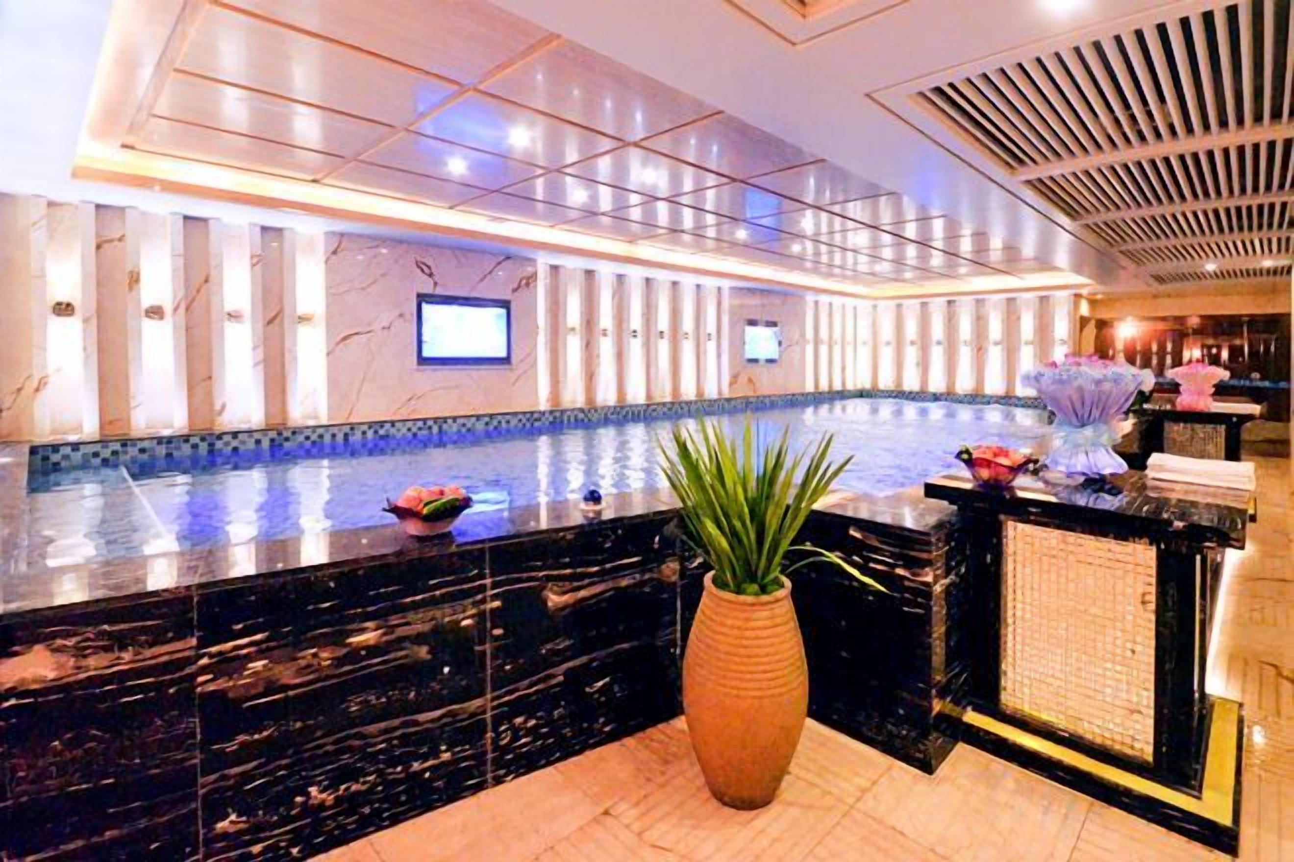 A hotel lobby with a reception desk, a large potted plant, and a pool area.