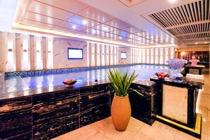 Un vestíbulo de hotel con una recepción, una planta grande en maceta y una zona de piscina.