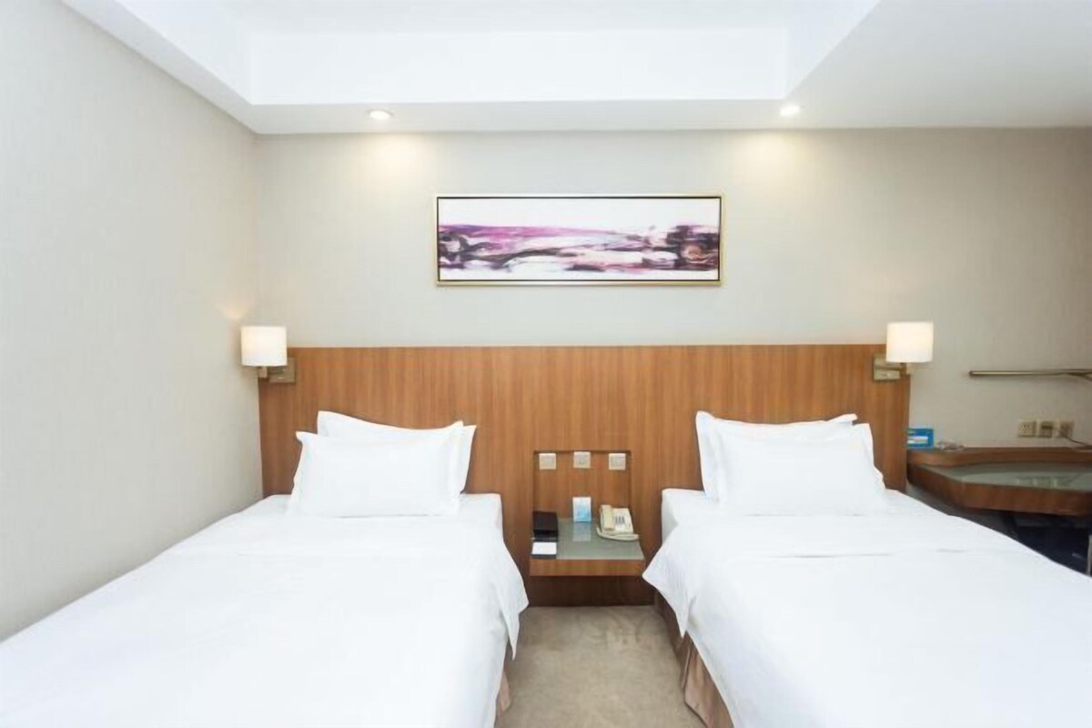 A hotel room with two beds, a wooden headboard, a nightstand with a phone, and a painting on the wall.