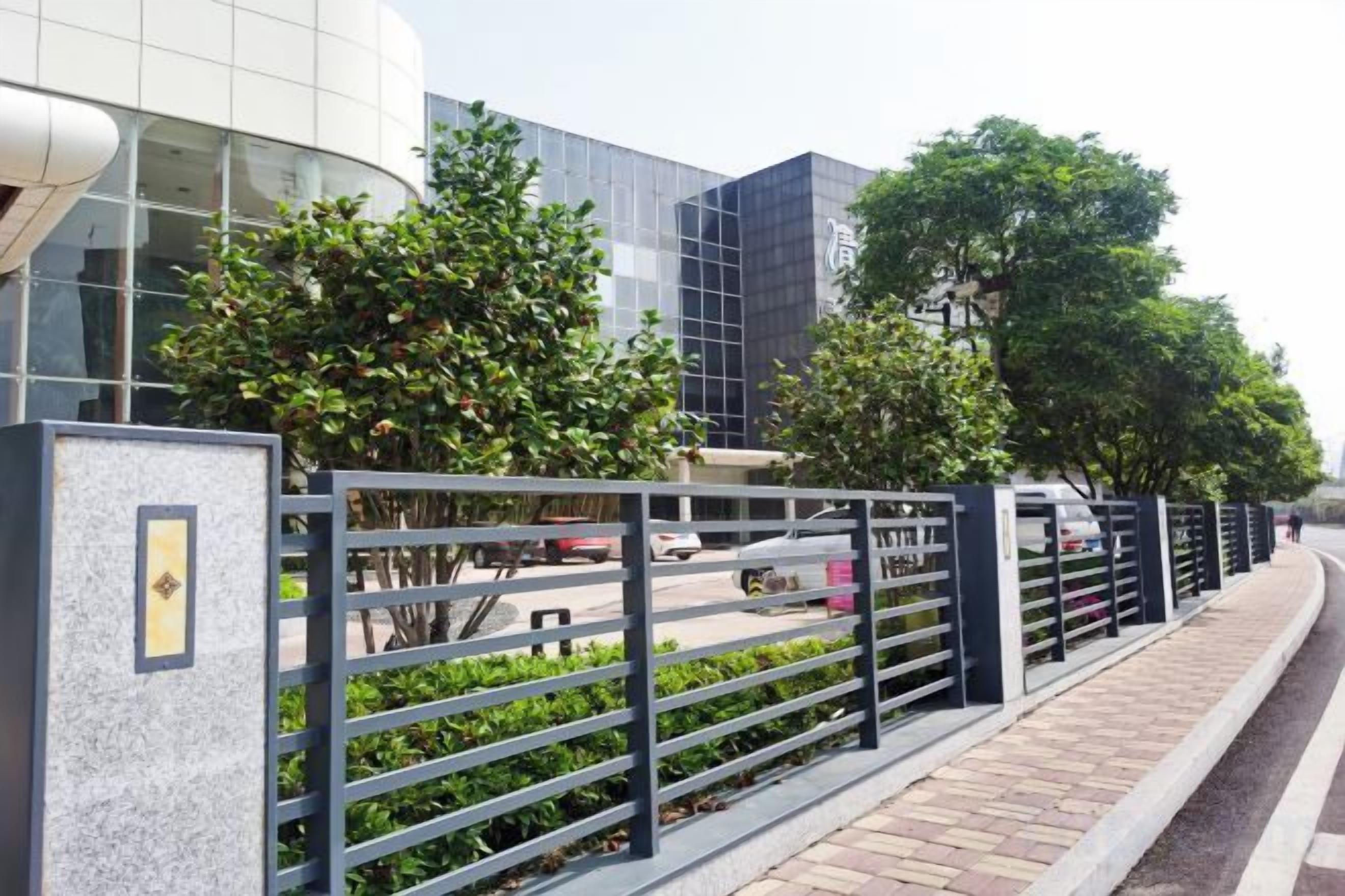 A modern building with a curved facade, a metal fence, and trees in the foreground.