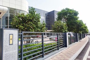 A modern building with a curved facade, a metal fence, and trees in the foreground. - Jinling Danyang Hotel (Danyang)