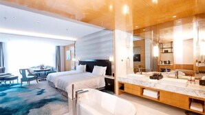 A modern hotel room with a large bed, a separate bathroom with a bathtub, a seating area with a table and chairs, and a large mirror. - Jinling Danyang Hotel (Danyang)