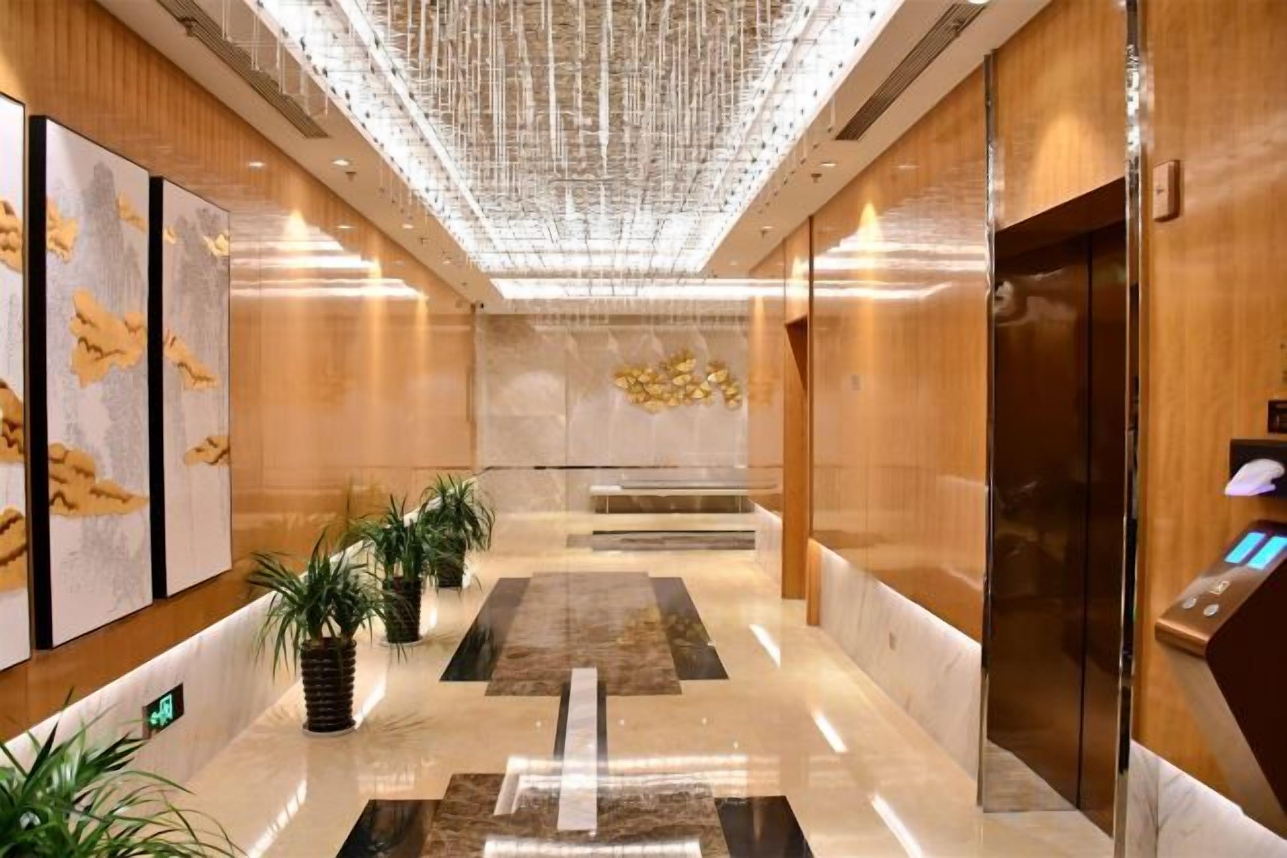 A modern lobby with a marble floor, wooden paneling, and a central elevator.