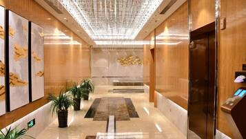 A modern lobby with a marble floor, wooden paneling, and a central elevator.
